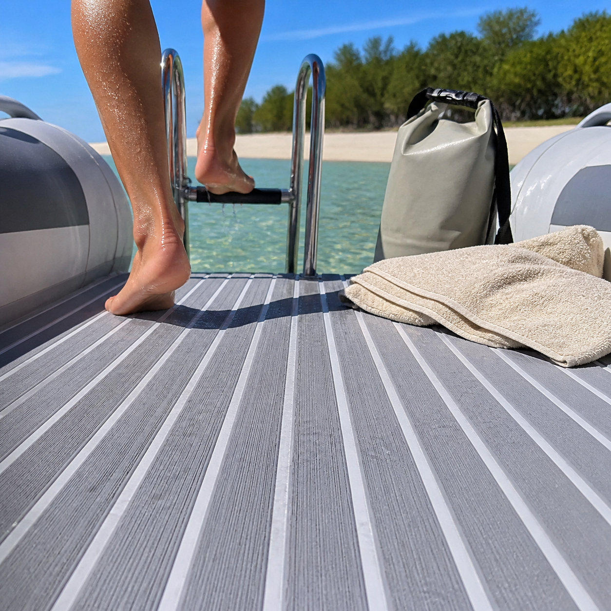 Wet boarding deck on a rigid inflatable boat with gray and white striped flooring, a metal swim ladder, bare feet, folded towels, and a dry bag