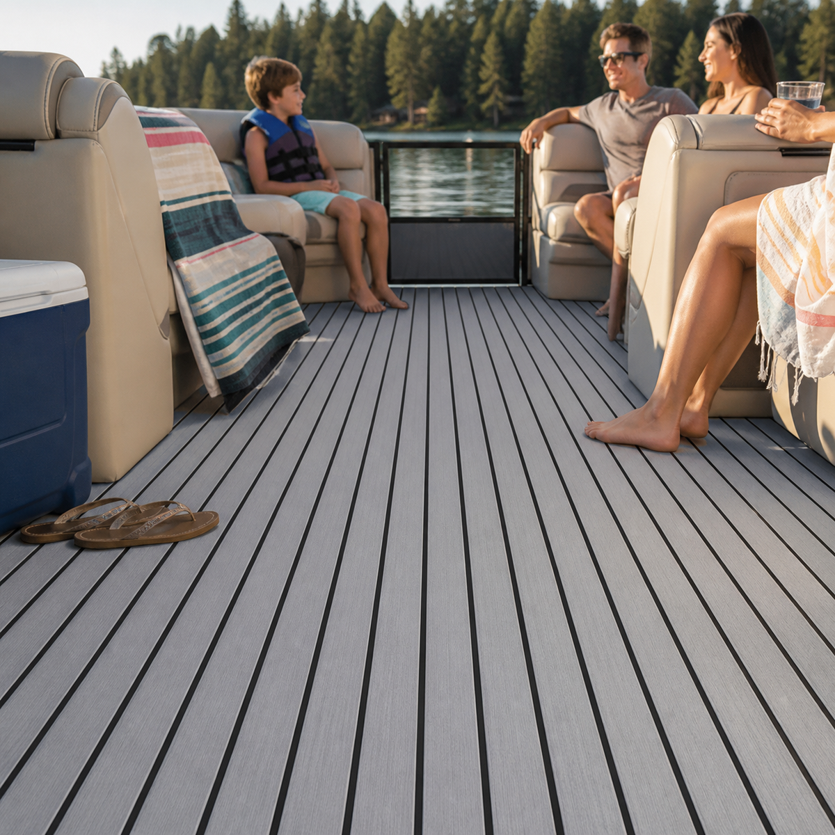 Pontoon seating area with light gray striped deck flooring, a side gate, a blue cooler, towels, sandals, and a family relaxing on a lake